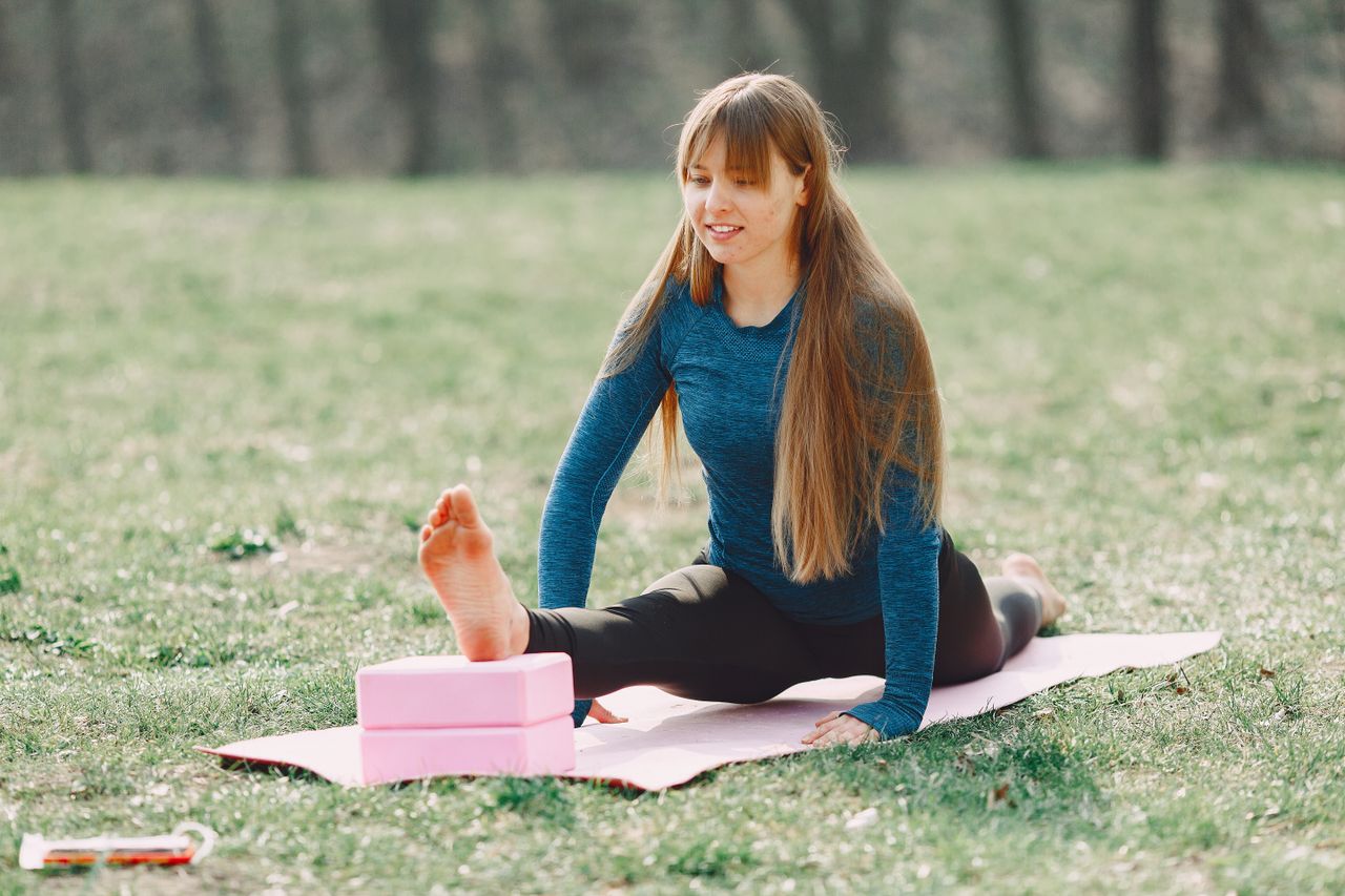 about-01 Smiling barefoot sportswoman in sportswear doing yoga leg exercise on sport mat during training on lawn in park adhering to healthy lifestyle while looking down