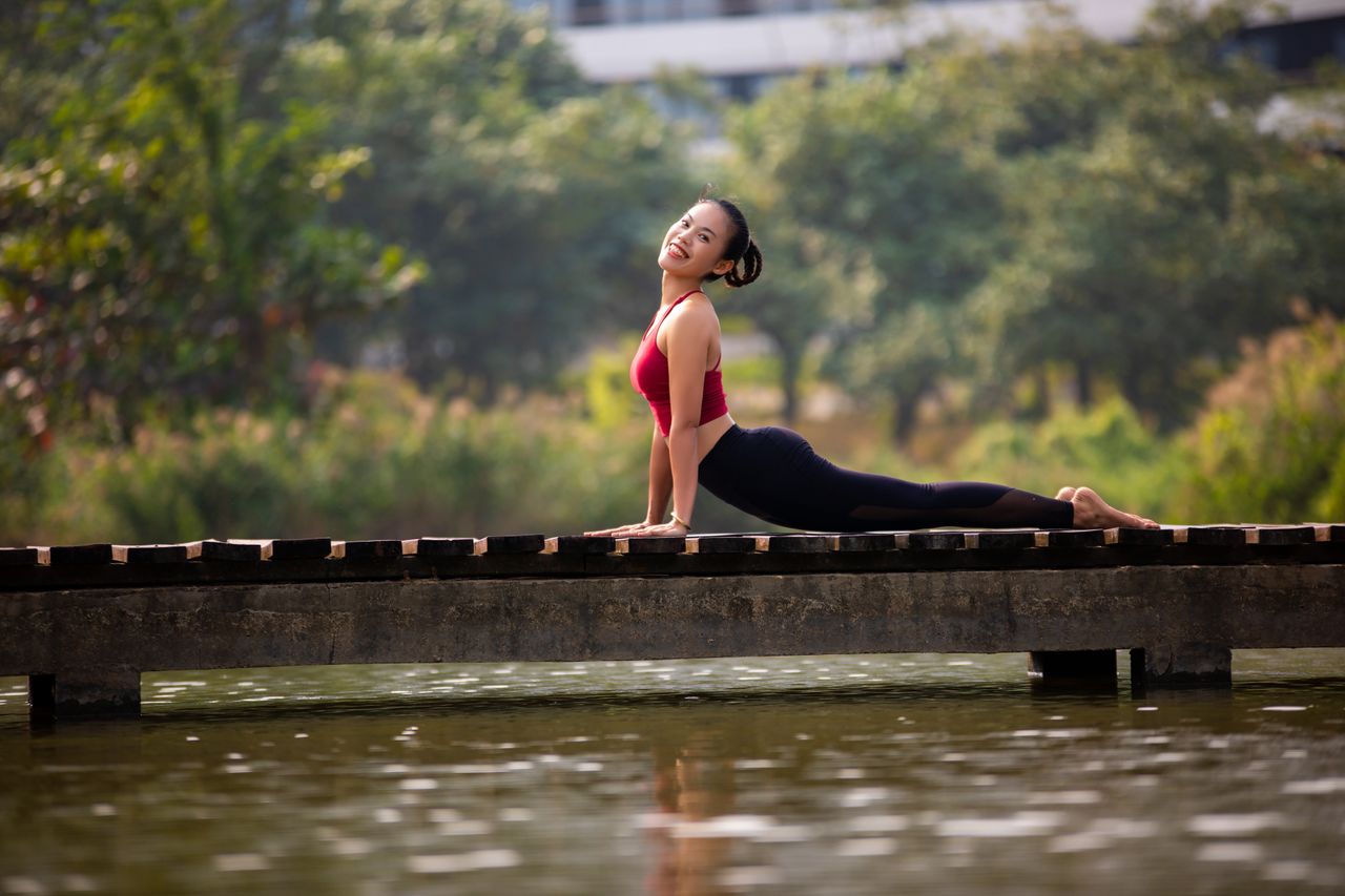 about-02 A woman enjoys a yoga pose on a bridge, showcasing flexibility and relaxation in a natural setting.