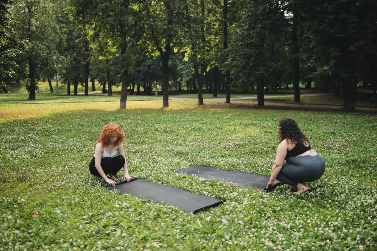 Mastering the First Impression: Your intriguing post title goes here Two women prepare yoga mats in a vibrant green park setting, perfect for outdoor fitness.