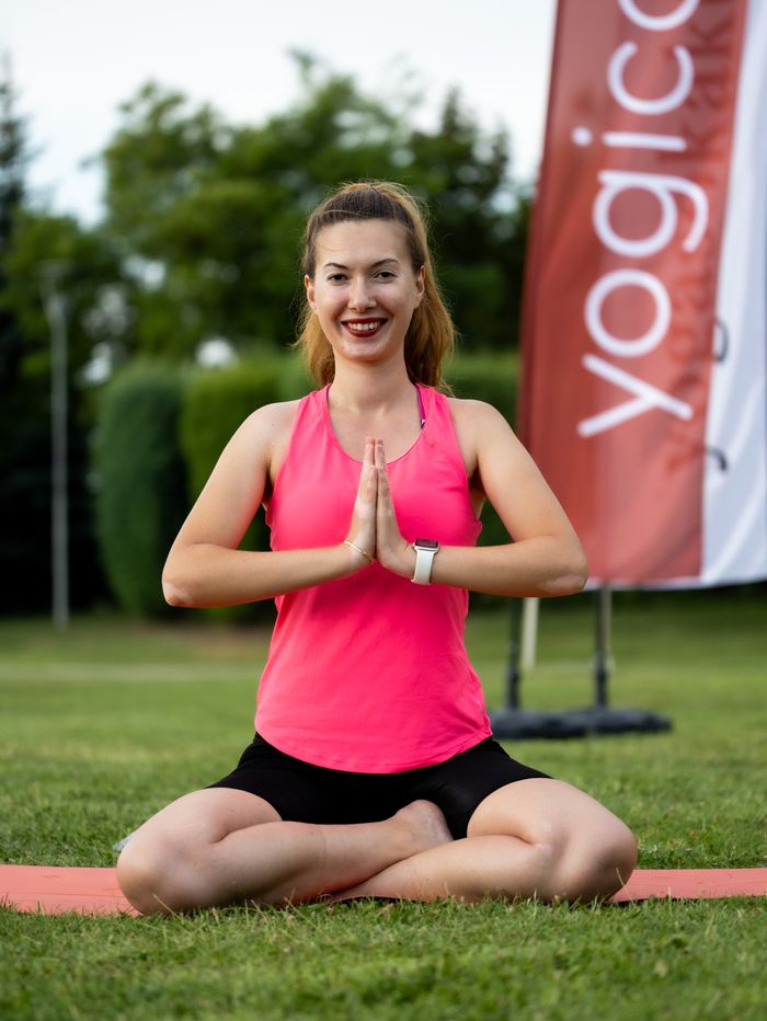 service-01 Smiling woman performing yoga on grass with hands in prayer position, embodying peaceful mindfulness outdoors.